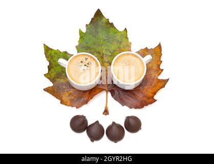 Two coffee cups and chocolate candies on a large pigmented maple leaf isolated on white Stock Photo
