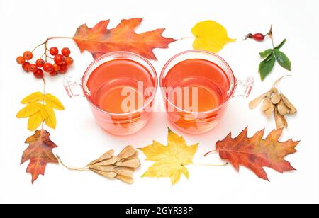 Two glass mugs with of hot beverages framed with bright autumn leaves and berries isolated on white. Cosy fall still life. Stock Photo