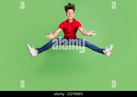 Photo of pretty impressed young guy dressed red t-shirt jumping high smiling isolated green color background Stock Photo