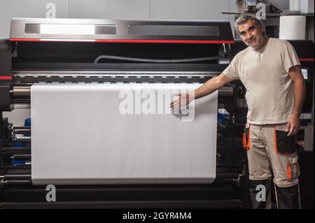 Technician worker operator show and point blank empty space of white paper on large premium industrial printer and plotter machine in digital printsho Stock Photo