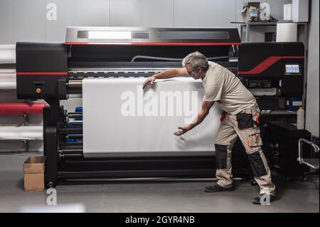 Technician worker operator show and point blank empty space of white paper on large premium industrial printer and plotter machine in digital printsho Stock Photo