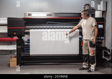 Technician worker operator show and point blank empty space of white paper on large premium industrial printer and plotter machine in digital printsho Stock Photo