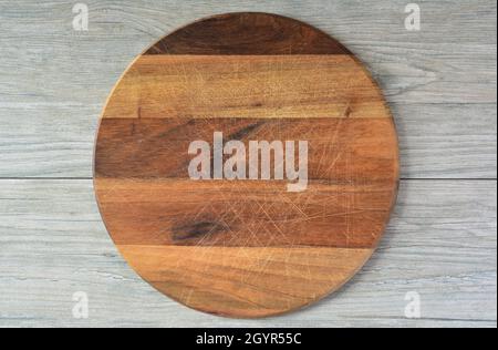 Empty round wooden chopping board made from dark nutwood, placed on light wooden kitchen table, top view Stock Photo