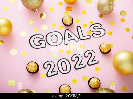 2022 Goals text with Christmas decorations gold confetti on pink color background. Goals 2022 lettering in Happy New Year style Stock Photo