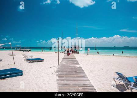 Tourists enjoying beach summer holiday with boats moored on pier Stock Photo