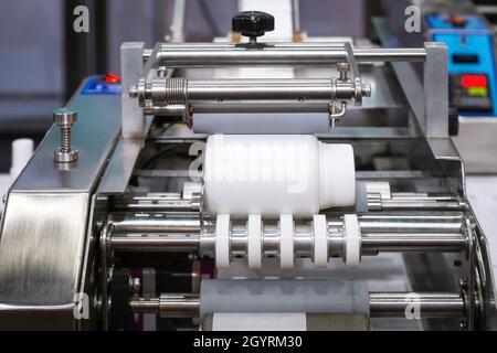 White plastic bottle on small tabletop bottle sticker labeling machine for medicine and pharmaceutical industry. Stock Photo
