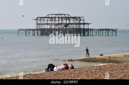 Brighton UK 9th October 2021 - Sunbathers relax in the sunshine on Brighton beach with some parts of the South East forecast to reach over 20 degrees centigrade : Credit Simon Dack / Alamy Live News