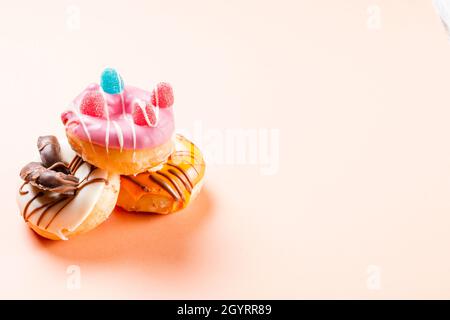 Photograph of three donuts decorated with jelly beans and drawn with chocolate.The photo is taken in horizontal format on a cream-colored background.T Stock Photo