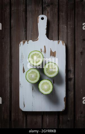 Cut green lemon on white wooden cutting board. Stock Photo