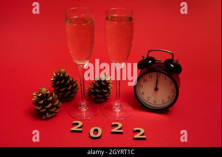 Christmas and New Year concept. Champagne flutes with sparkling wine, alarm clock showing midnight in the face clock, golden pine cones and wooden num Stock Photo