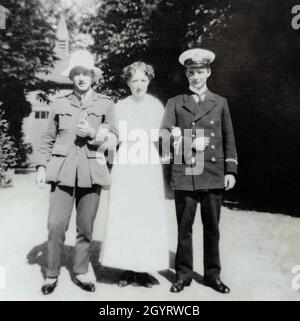 A First World War era portrait of a mother standing he her sons, officers in uniform. The man on the left compliments his British army officer uniform with what looks to be womans shoes and hat. The man on the right has kept a more regulation look in the uniform of a Sub-lieutenant in the Royal Navy. Stock Photo