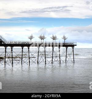 Royal Pier, Aberystwyth, Wales, UK. Decorative imitation trees outlined at the end of the pier. Blue sky with clouds above and calm sea below Stock Photo