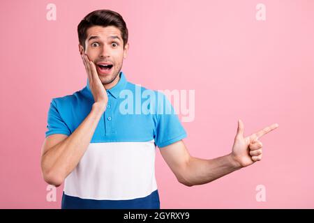Photo of impressed brunet young guy point empty space wear blue t-shirt isolated on pink color background Stock Photo