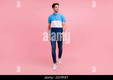 Full size photo of optimistic brunet young guy go look empty space wear polo jeans sneakers isolated on pink background Stock Photo