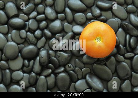 Tomato on black stone that has smooth glossy skin and round edge. Black stone background make tomato look standout. Stock Photo