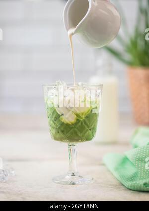 Cold Matcha green tea with ice cube and milk. Healthy eating concept. Pouring milk into a glass of green tea. With copy space for text. Stock Photo