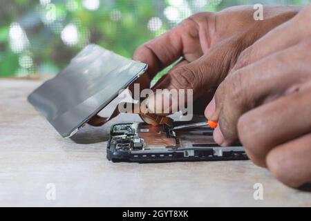 Phone motherboard part repairs into the motherboard for smartphone By professional technician on a table With green nature background. Stock Photo