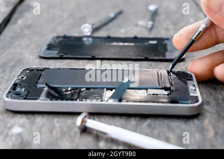 The technician holding a screwdriver a mobile phone repair Closeup inside cell phone with a fixing battery from a broken service shop center on wood t Stock Photo