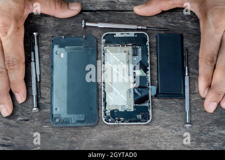 Top view of the hand technician with a screwdriver mobile phone repair inside a cell phone with a fixing battery from a broken service shop center on Stock Photo