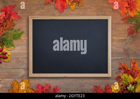 Clean chalkboard on wooden table surrounded by autumn leaves. Top view, flat lay composition Stock Photo