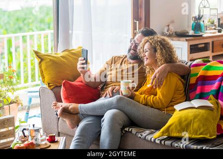 Happy couple having fun and embracing while taking selfie on mobile phone sitting on sofa.Happy caucasian couple spending leisure time together while Stock Photo