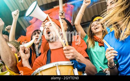 Fan supporters friends cheering and watching soccer cup match at intenational stadium - Young people group with multicolored tshirts having excited fu Stock Photo