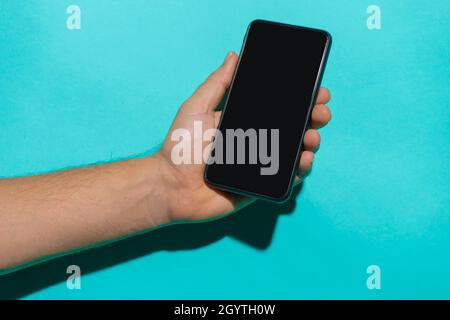 Smartphone mockup with man hand holding the phone in front of a colorful blue background with copy space for text. Stock Photo