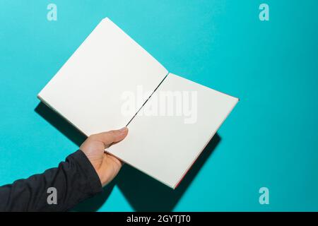 Hand holding open book with clean white pages in front of blue background with copy space for text. Stock Photo
