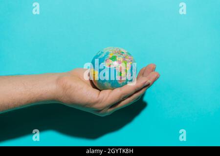 Hand holding globe ball in colorful blue background with copy space for text. Stock Photo