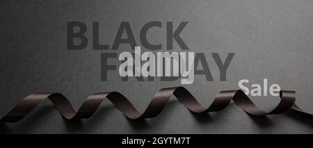 Black Friday Sale text lettering and curly ribbon, dark background. Special seasonal offers sign. Banner, website header Stock Photo