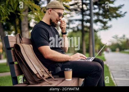 Stylish millennial bearded man chatting working e-learning laptop at green park Distance education  Stock Photo