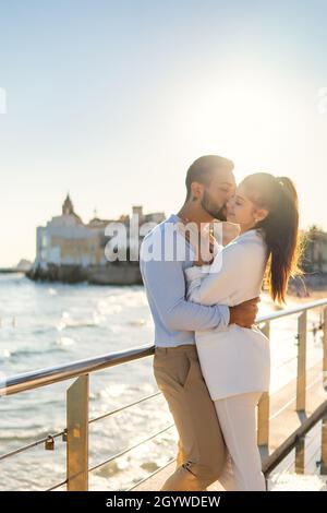 Side view of romantic ethnic couple standing near railing on promenade and embracing gently on sunny day in summer Stock Photo