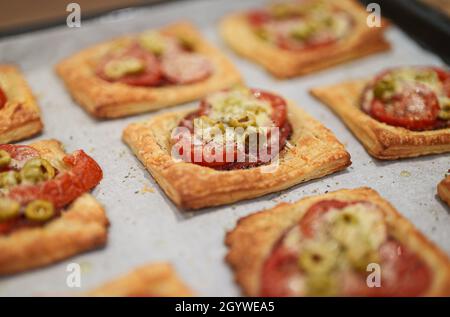 Baked square mini pizzas with salami, cheese, olives and tomato. Stock Photo