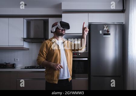 The young man who entered the world of the metaverse from the kitchen. touching with vr glasses. Stock Photo