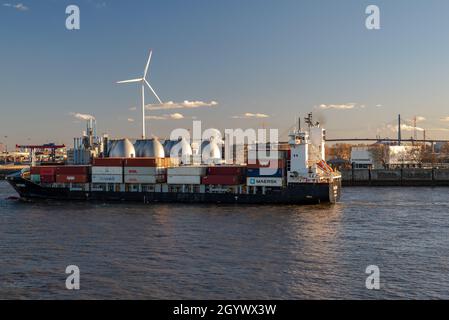 Hamburg, Germany-05.03.2021:small container freighter on the river elbe and in the background a wind turbine and the köhlbrand bridge Stock Photo