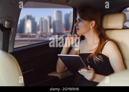Elegant business woman using tablet computer inside a car on rear seat or vip taxi. Stock Photo