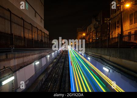 Colorful blue, yellow, green and red light trails from the CTA holiday train coming out of tunnel at night with alley lights and residential buildings Stock Photo