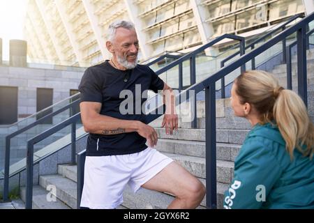 Fit mature couple chatting while standing outdoors after morning workout in the city Stock Photo