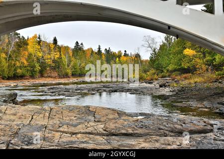 A river with a low level of water flowing over rocks, because of little rain in summer, exposing more large rocks, while trees are showing fall color. Stock Photo