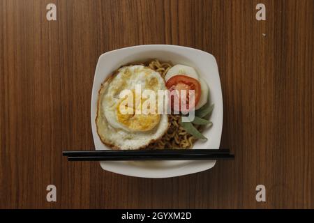 Fried noodles, eggs, tomatoes, and cucumbers as accompaniments placed on a wooden table. Stock Photo
