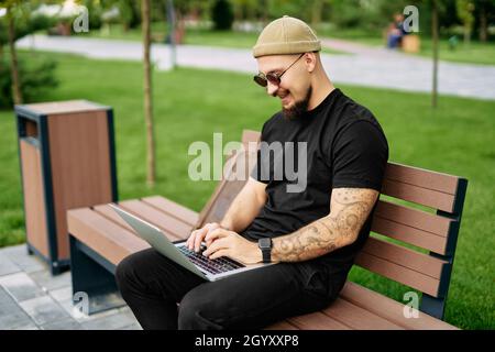 Stylish bearded millennial chatting working e-learning laptop at green park Distance education  Stock Photo