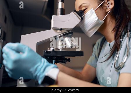 Asian doctor with medical mask and gloves looks into microscope at table in laboratory Stock Photo