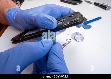 the master repairs a broken smartphone with the help of tools. Stock Photo