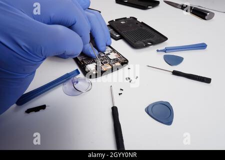 the master repairs a broken smartphone with the help of tools. Stock Photo