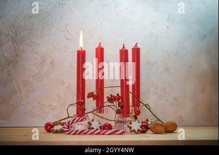 Four red candles, one is lit for the first Sunday before Christmas, Advent decoration on a wooden table against a rustic wall, copy space, selected fo Stock Photo