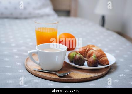 Breakfast in bed. Croissant on a plate with figs, a coffee cup, orange juice and an orange on a tray. Stock Photo