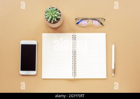 Blank notepad, pen, smartphone, glasses and potted plant on beige table. Top view, flat lay, mock up. Stock Photo