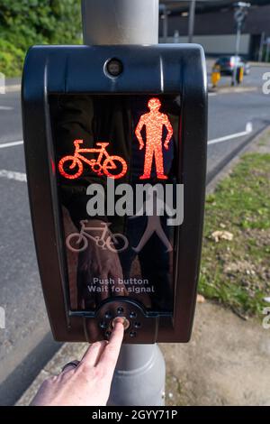 A man's finger pushing a button on a pedestrian crossing signal on red man 'Do Not Cross' next to a busy road in Basingstoke, UK Stock Photo