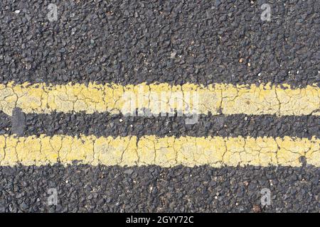 Double yellow lines in thermoplastic paint on an asphalt road in England that prohibit parking and waiting at any time Stock Photo