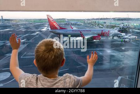 Newcastle Airport, UK. 10th Oct, 2021. A young boy looks out from the departure lounge at Newcastle Airport to a Jet2 and TUI planes on the departure gates before taking off with holiday makers heading for half term sunshine as the travel industry starts a slow recovery from the covid pandemic and testing for Coronavirus measures are becoming easier and cheaper over the coming weeks. picture Credit: phil wilkinson/Alamy Live News Stock Photo